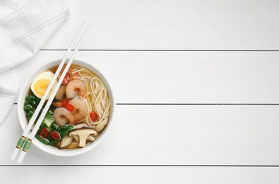 Photo of Tasty ramen with shrimps in bowl and chopsticks on white wooden table, top view. Space for text