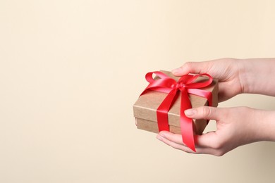 Photo of Woman holding gift box with red bow on beige background, closeup. Space for text