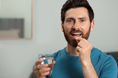 Photo of Handsome man with glass of water taking pill indoors, space for text