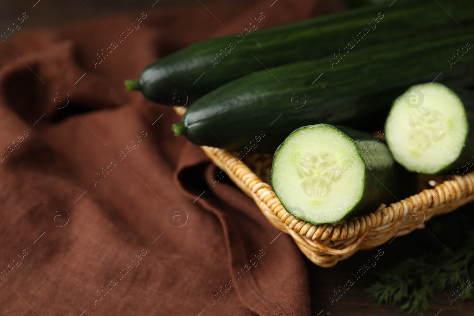 Photo of Fresh cucumbers in wicker basket on table, closeup. Space for text