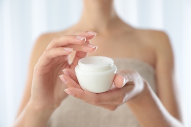 Photo of Young woman holding jar of cream at home, closeup