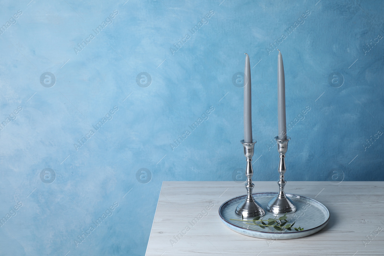 Photo of Holders with candles on wooden table near light blue wall, space for text