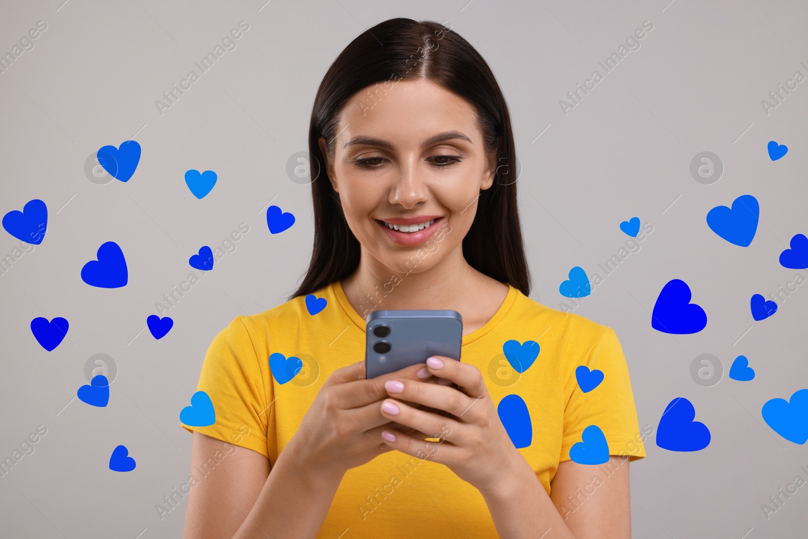 Image of Long distance love. Woman chatting with sweetheart via smartphone on grey background. Hearts flying out of device and swirling around her