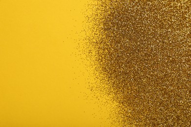 Photo of Shiny golden glitter on yellow background, top view. Space for text