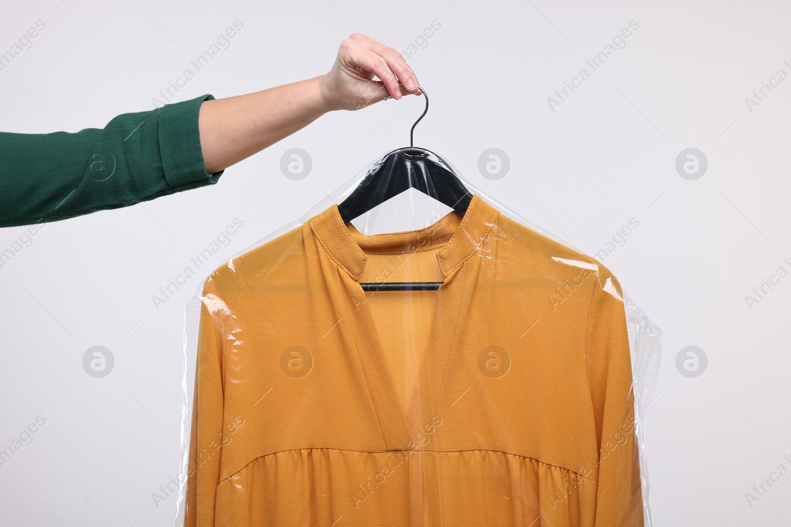 Photo of Dry-cleaning service. Woman holding dress in plastic bag on white background, closeup