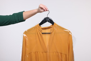 Photo of Dry-cleaning service. Woman holding dress in plastic bag on white background, closeup