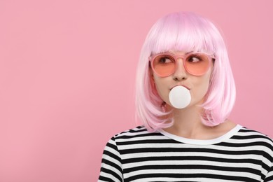 Beautiful woman in sunglasses blowing bubble gum on pink background, space for text