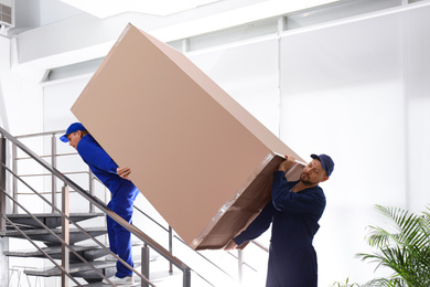 Photo of Professional workers carrying refrigerator on stairs indoors