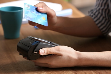 Woman using modern payment terminal at table indoors, closeup