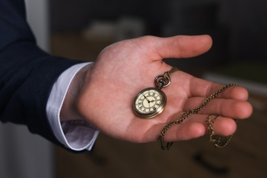 Photo of Man holding chain with elegant pocket watch on blurred background, closeup
