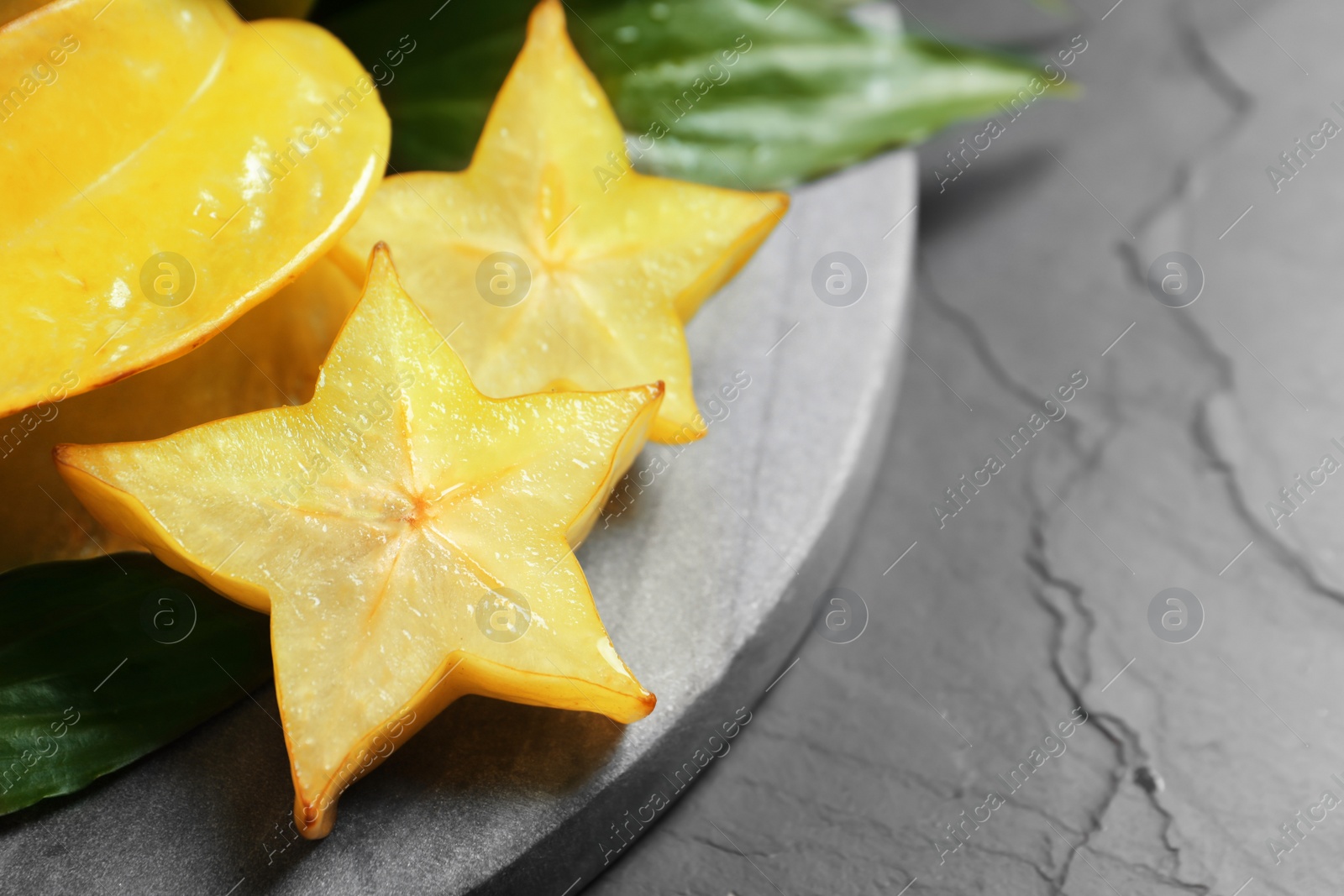 Photo of Cut and whole carambolas on black slate table, closeup. Space for text