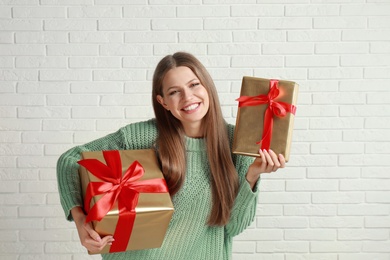 Photo of Happy young woman with Christmas gifts near white brick wall