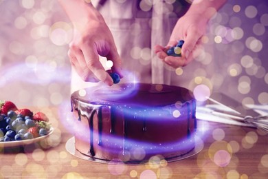 Woman decorating fresh delicious homemade chocolate cake with berries at table, closeup Tasty dessert for Christmas dinner