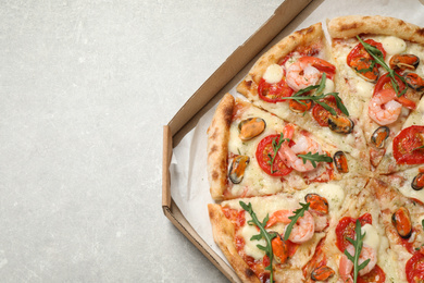 Photo of Delicious seafood pizza in box on light grey table, top view. Space for text