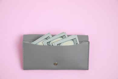 Photo of Stylish grey leather purse with dollar banknotes on pink background, top view. Space for text