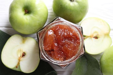 Photo of Glass jar of delicious apple jam and fresh fruits on white wooden table, flat lay