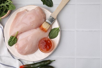 Marinade, basting brush and raw chicken fillets on white table, flat lay. Space for text