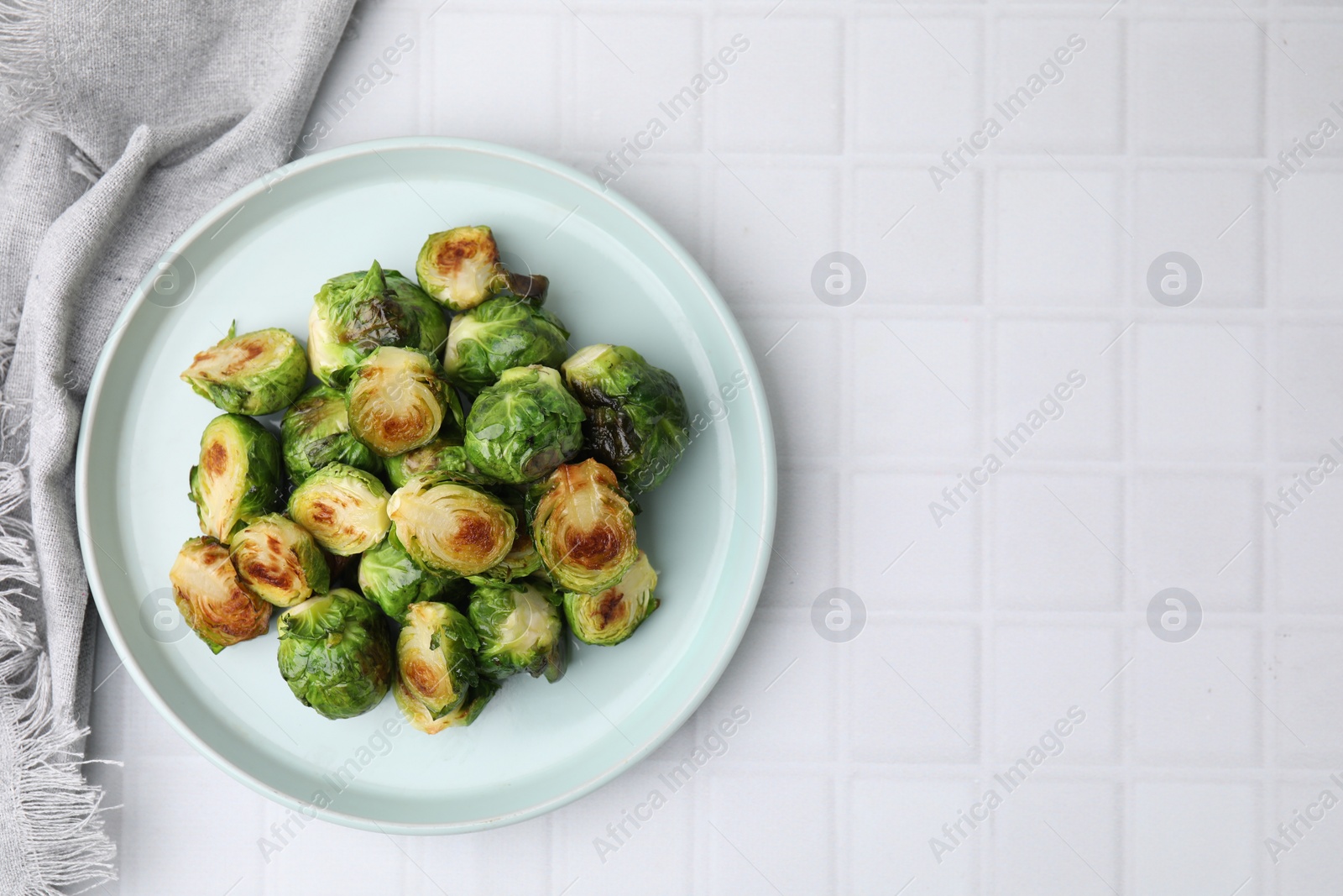 Photo of Delicious roasted Brussels sprouts on white tiled table, top view. Space for text