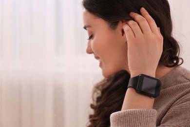 Young woman with smart watch at home, space for text