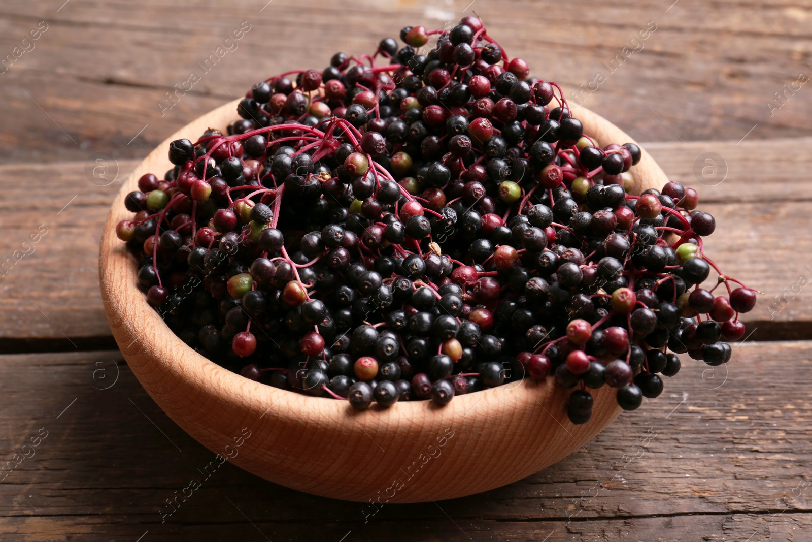 Photo of Bowl with tasty elderberries (Sambucus) on wooden table, closeup