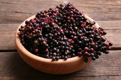 Photo of Bowl with tasty elderberries (Sambucus) on wooden table, closeup