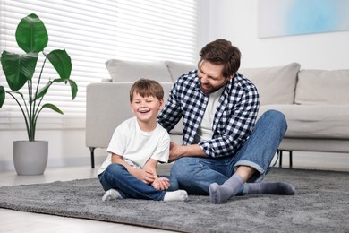 Photo of Happy dad and son having fun on carpet at home