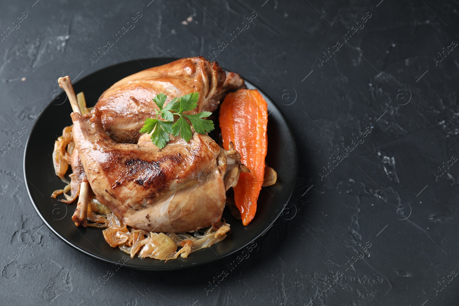 Photo of Tasty cooked rabbit meat with vegetables and parsley on black table, space for text