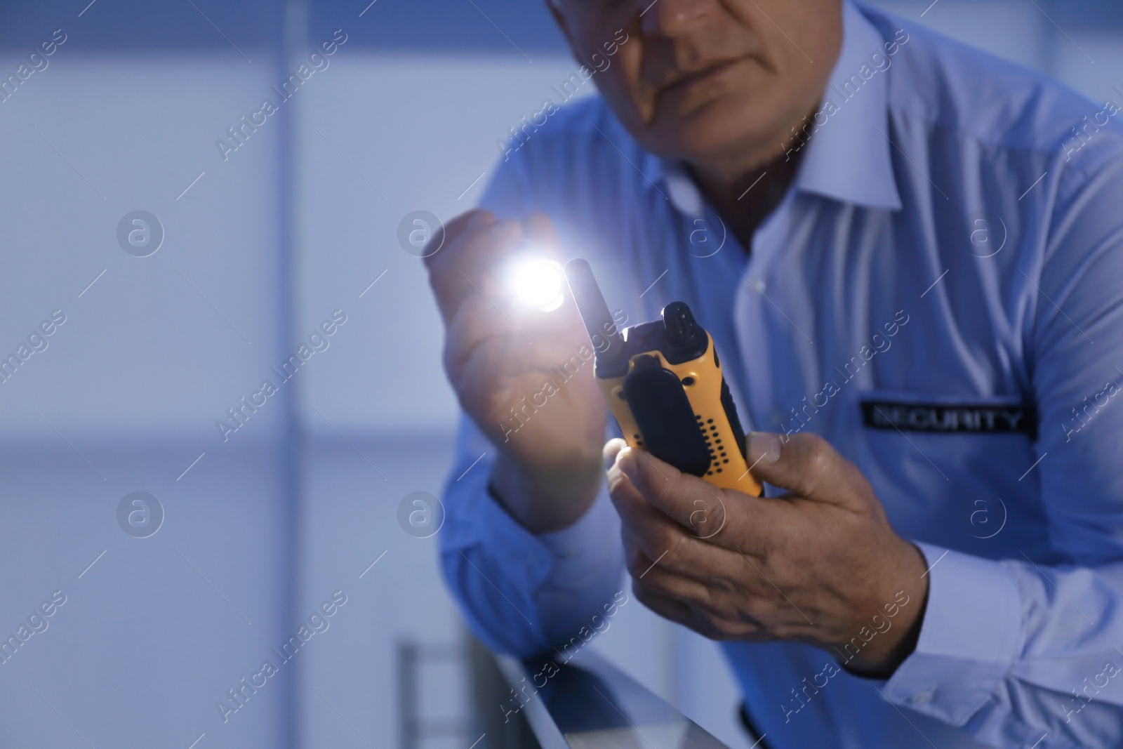 Photo of Professional security guard with portable radio set and flashlight in dark room, closeup