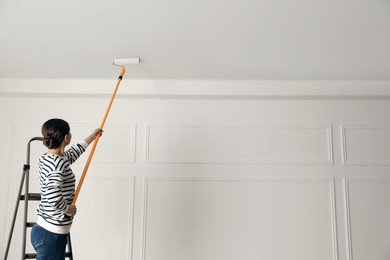 Photo of Young woman painting ceiling with white dye indoors, back view. Space for text