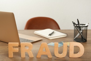 Photo of Word Fraud made of wooden letters near laptop and stationery on office desk