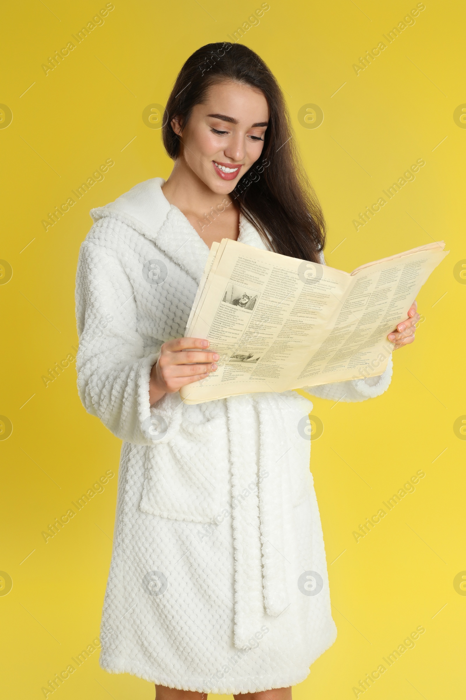 Photo of Beautiful young woman in bathrobe reading newspaper on yellow background