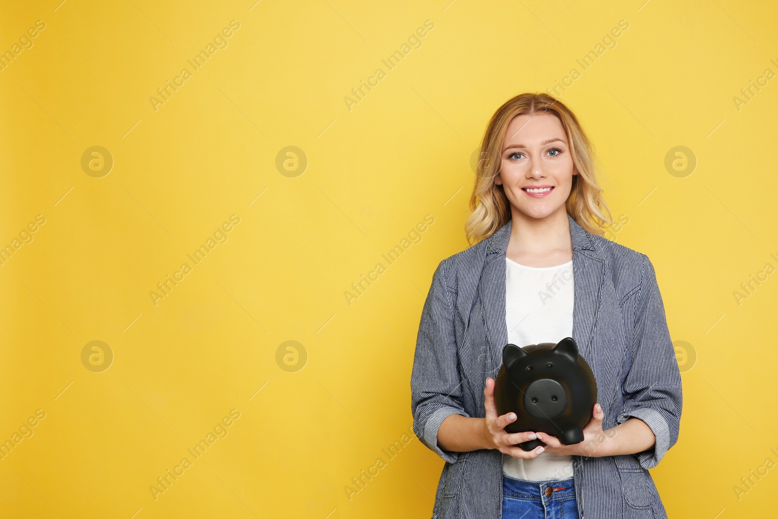 Photo of Happy young woman with piggy bank on color background. Space for text