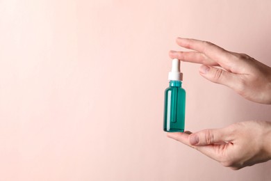 Photo of Woman with bottle of cosmetic serum on light pink background, closeup. Space for text