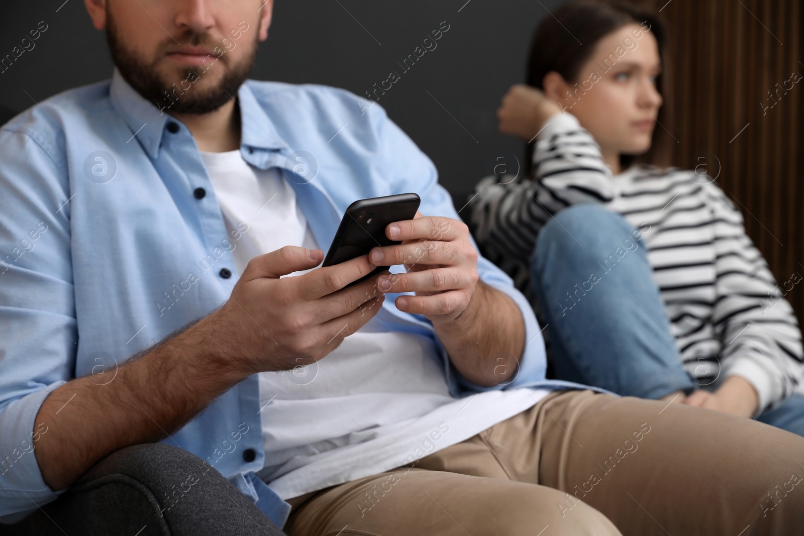 Photo of Man with smartphone ignoring his girlfriend at home, closeup. Relationship problems