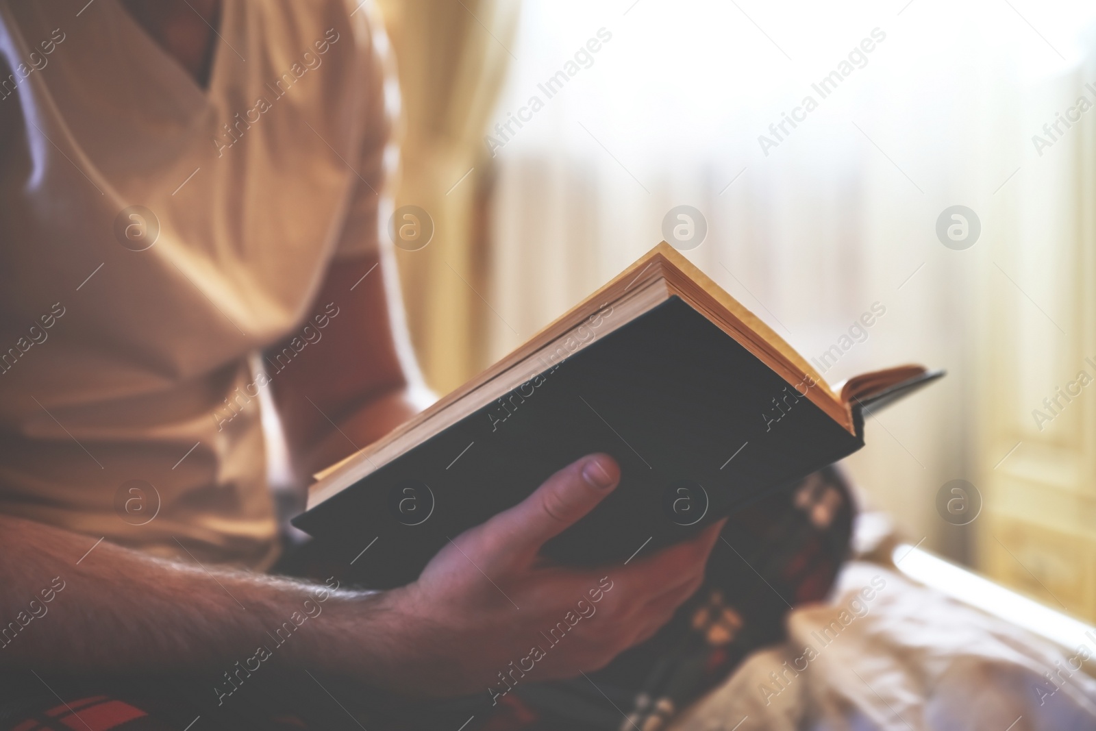 Photo of Young man reading book on bed at home, closeup