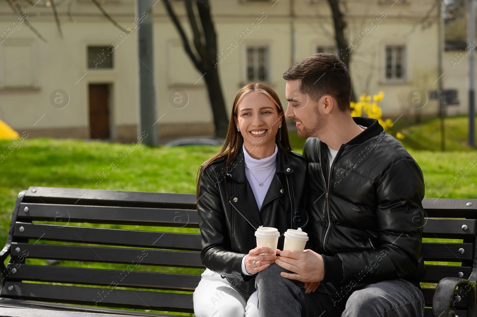 Photo of Lovely young couple with cups of coffee on bench outdoors. Romantic date