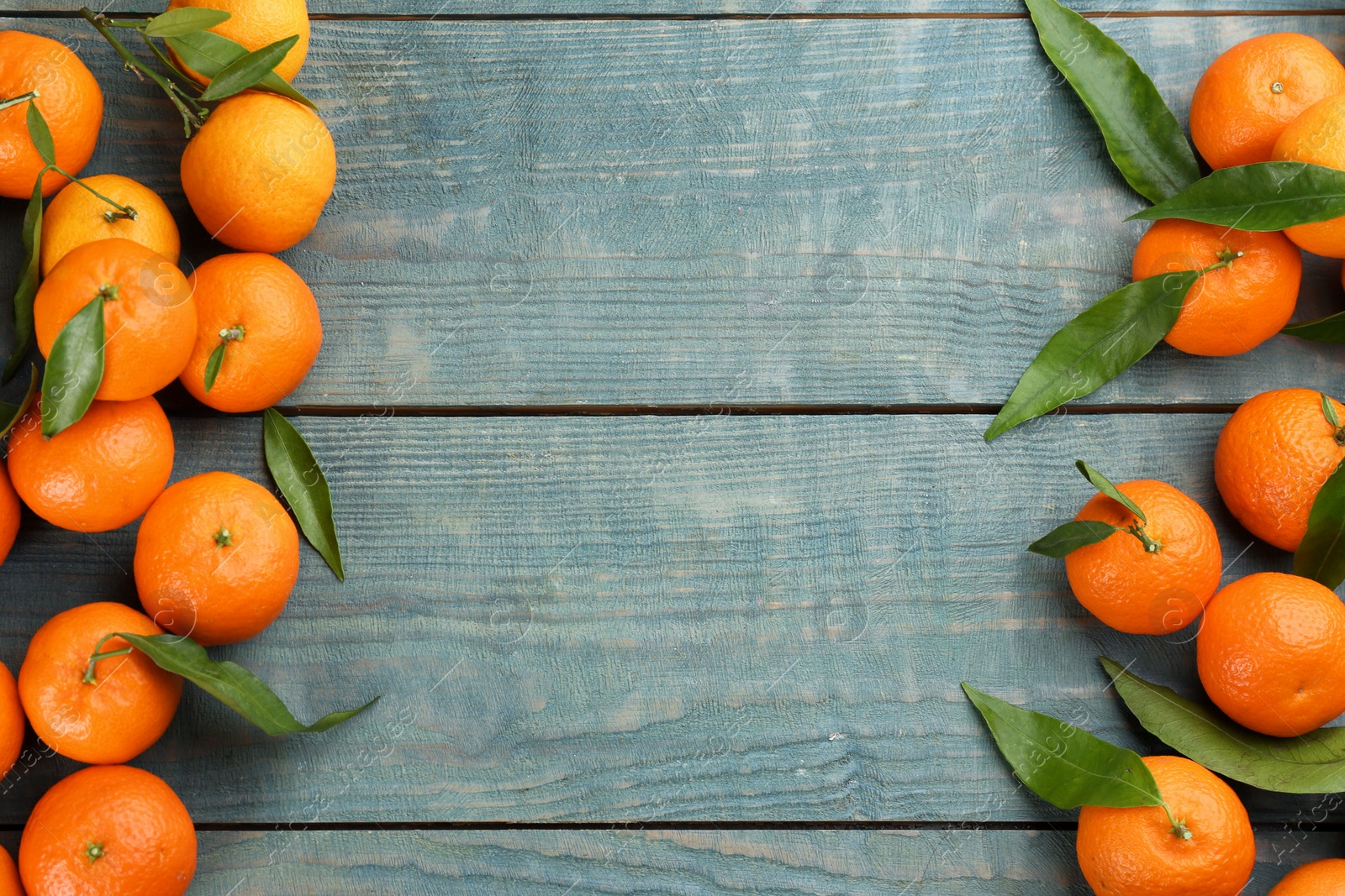 Photo of Fresh ripe tangerines with green leaves on blue wooden table, flat lay. Space for text