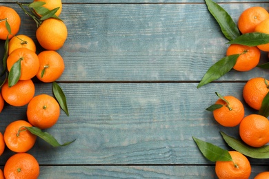 Fresh ripe tangerines with green leaves on blue wooden table, flat lay. Space for text