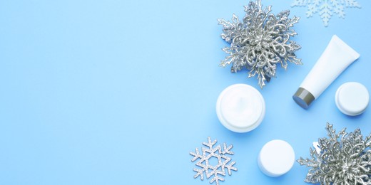 Image of Winter skin care. Flat lay composition with cosmetic products and snowflakes on light blue background, space for text. Banner design