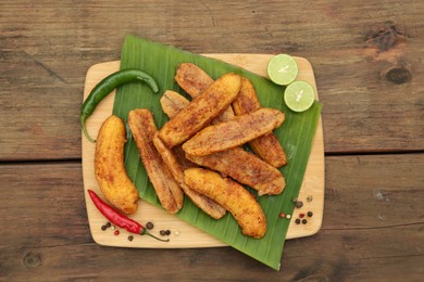 Delicious fried bananas, different peppers and cut limes on wooden table, top view