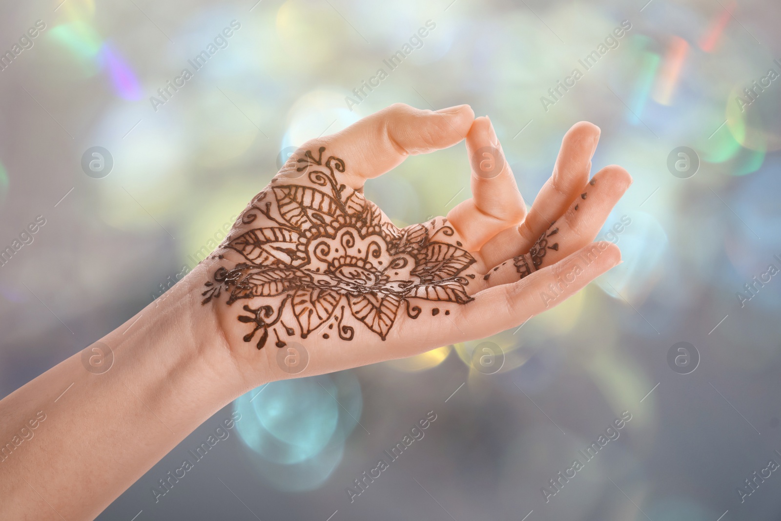 Image of Woman with henna tattoo on palm against blurred lights, bokeh effect