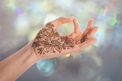 Image of Woman with henna tattoo on palm against blurred lights, bokeh effect