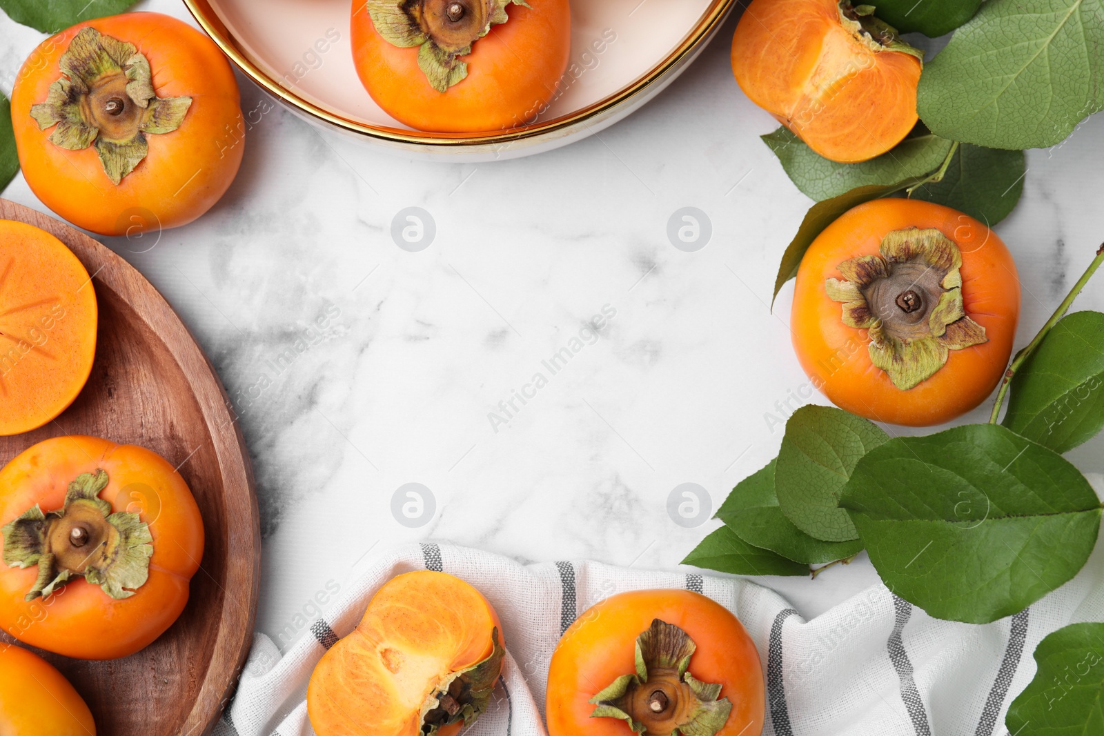 Photo of Whole and cut delicious ripe juicy persimmons with green leaves on white marble table, flat lay. Space for text