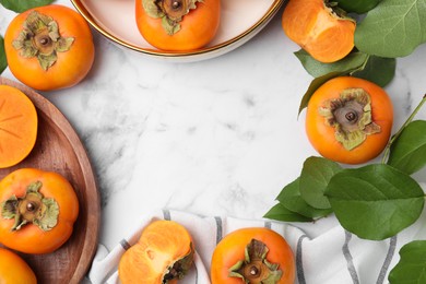 Whole and cut delicious ripe juicy persimmons with green leaves on white marble table, flat lay. Space for text