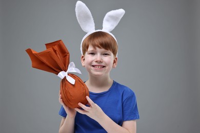 Photo of Easter celebration. Cute little boy with bunny ears and wrapped egg on grey background