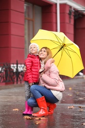 Mother and daughter with umbrella in city on autumn rainy day