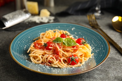 Photo of Tasty pasta with basil, tomatoes and cheese on grey table