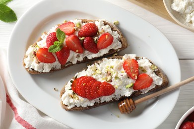 Photo of Delicious ricotta bruschettas with strawberry, mint and pistachios served with honey on white wooden table, flat lay