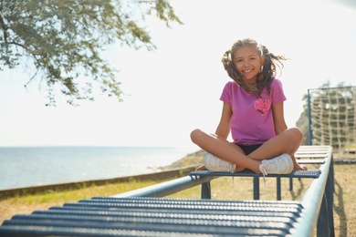 Photo of Cute girl on playground climber outdoors. Summer camp