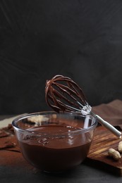 Bowl of chocolate cream and whisk on table against dark background, space for text